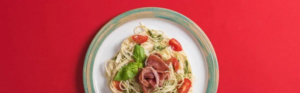 Vista dall'alto delle Pappardelle cotte con pomodori, basilico e prosciutto su piatto su fondo rosso, colpo panoramico — Foto stock