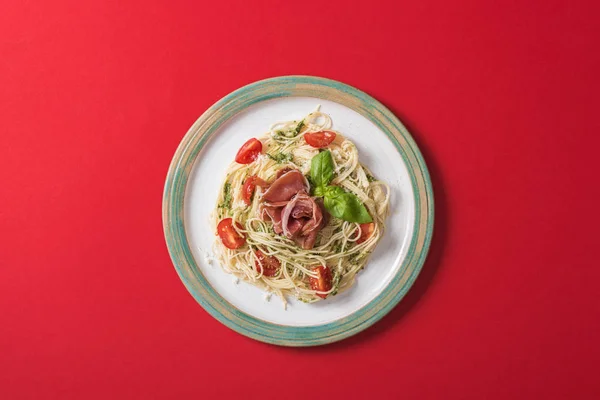 Draufsicht auf gekochte Pappardelle mit Tomaten, Basilikum und Prosciutto auf Teller auf rotem Hintergrund — Stockfoto