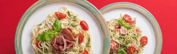 Top view of cooked Pappardelle with tomatoes, basil and prosciutto on plates on red background, panoramic shot — Stock Photo