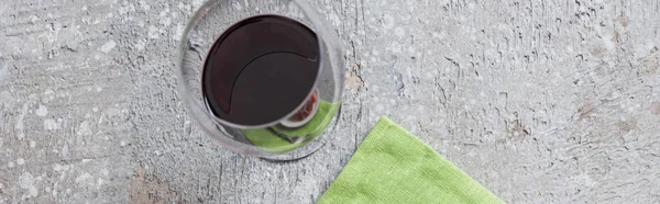 Vue du dessus du verre de vin rouge près de la serviette verte sur la surface grise, vue panoramique — Photo de stock