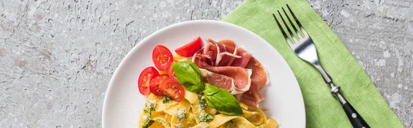 Vista dall'alto delle Pappardelle cotte con pomodori, basilico e prosciutto vicino al bivio su superficie grigia, colpo panoramico — Foto stock