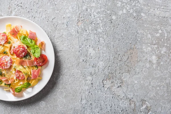 Top view of cooked Pappardelle with tomatoes, pesto sauce and prosciutto on grey surface — Stock Photo