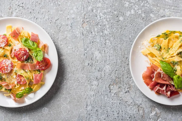 Top view of cooked Pappardelle with tomatoes, pesto sauce and prosciutto on grey surface — Stock Photo