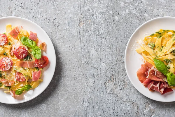 Vista superior de Pappardelle cocido con tomates, salsa de pesto y jamón sobre superficie gris - foto de stock