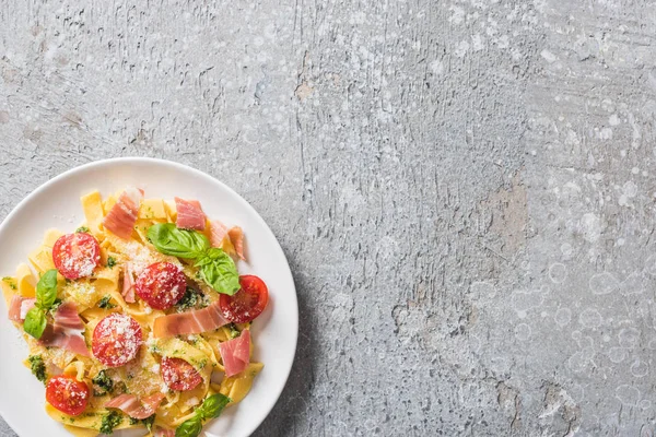 Top view of cooked Pappardelle with tomatoes, pesto sauce and prosciutto on grey surface — Stock Photo