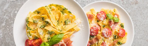 Selective focus of cooked Pappardelle with tomatoes, basil and prosciutto on plates on grey surface, panoramic shot — Stock Photo