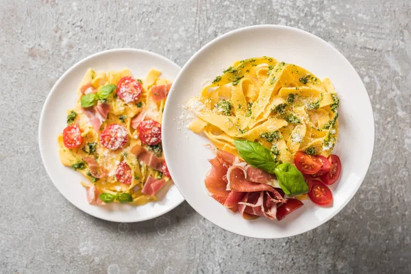 Enfoque selectivo de Pappardelle cocido con tomates, albahaca y prosciutto en platos en superficie gris - foto de stock