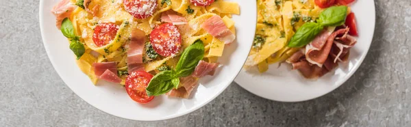 Селективный фокус приготовленного Папарделле с помидорами, базиликом и прошутто на тарелках на серой поверхности, панорамный снимок — стоковое фото