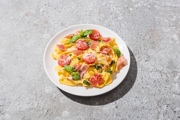 Tasty Pappardelle with tomatoes, pesto and prosciutto on grey surface — Stock Photo