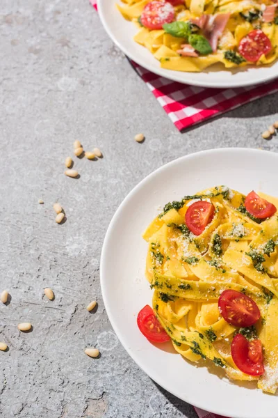 Leckere Pappardelle mit Tomaten, Pesto und Schinken mit Gabel in der Nähe von Rotwein, Basilikum und Pinienkernen auf grauer Oberfläche — Stockfoto