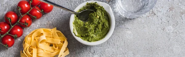 Vista superior de Pappardelle cru perto de tomates, água e molho pesto na superfície cinza, tiro panorâmico — Fotografia de Stock