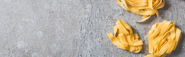 Top view of raw Pappardelle on grey surface, panoramic shot — Stock Photo