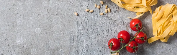 Vista superior de Pappardelle crudo cerca de tomates, piñones, parmesano en superficie gris, plano panorámico - foto de stock