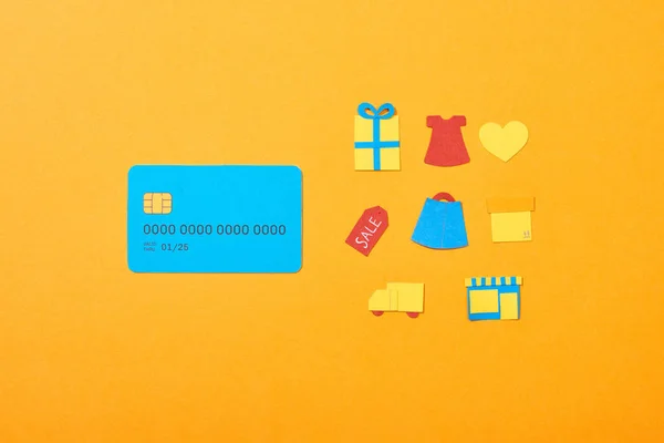 Piatto lay con modello di carta di credito blu vicino alle icone dello shopping isolato su arancione — Foto stock