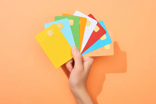 Cropped view of woman holding multicolored empty credit cards on peach background — Stock Photo