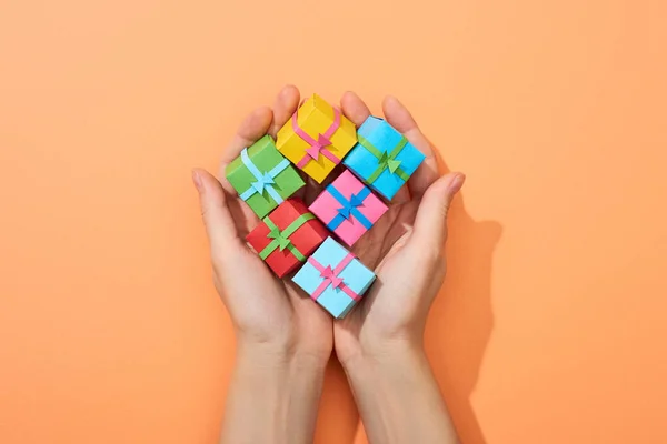 Vista recortada de la mujer sosteniendo pequeñas cajas de regalo multicolores sobre fondo de melocotón - foto de stock