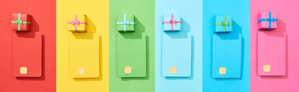 Top view of multicolored empty credit cards and gift boxes on rainbow background, panoramic shot — Stock Photo