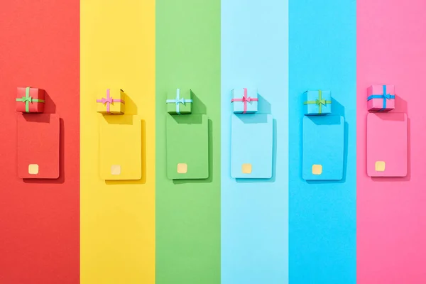 Vista superior de tarjetas de crédito vacías multicolores y cajas de regalo sobre fondo de arco iris - foto de stock