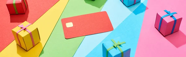 Tarjeta de crédito vacía roja y cajas de regalo multicolores sobre fondo de arco iris, plano panorámico - foto de stock