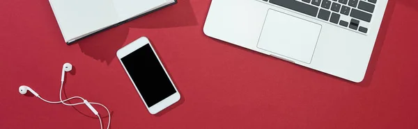 Top view of smartphone, laptop, earphones, blank notebook on red background, panoramic shot — Stock Photo