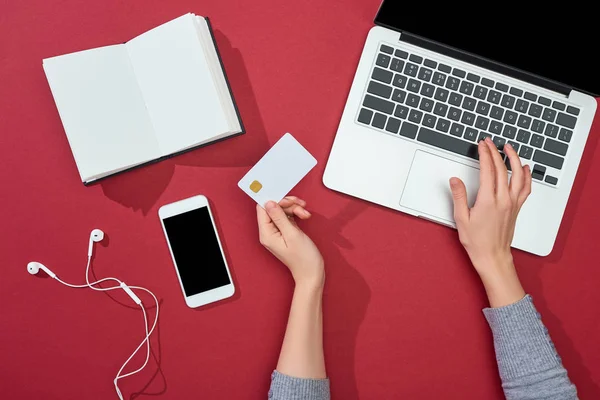 Top view of credit card on red background with smartphone, laptop, earphones, coffee, notebook and plant — Stock Photo