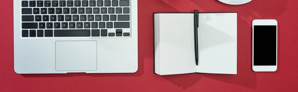 Plat avec smartphone, ordinateur portable, ordinateur portable avec stylo sur fond rouge, panoramique — Photo de stock
