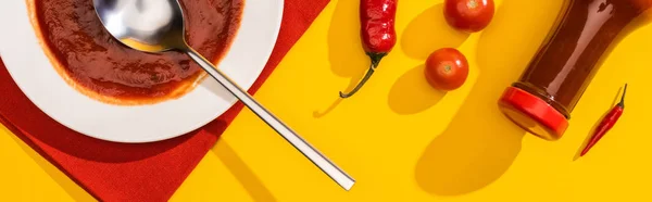 Top view of plate and bottle with ketchup, chili peppers and cherry tomatoes on yellow background, panoramic shot — Stock Photo