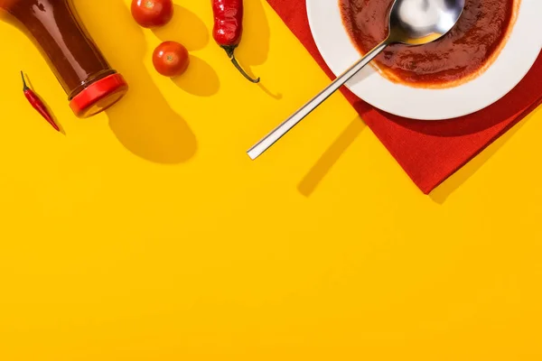 Vista superior de pimentas com tomate cereja, prato e garrafa com ketchup na superfície amarela — Fotografia de Stock