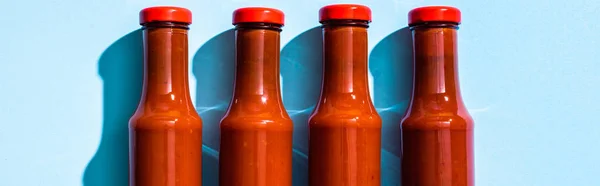 Vista superior de botellas con salsa de tomate sobre fondo azul, plano panorámico - foto de stock