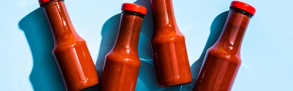 Vue du dessus des bouteilles avec sauce tomate savoureuse sur fond bleu, panoramique — Photo de stock