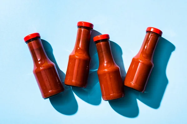 Vista superior de la salsa de tomate en botellas con sombra sobre fondo azul - foto de stock