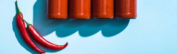 Vista dall'alto di bottiglie con salsa di peperoncino e peperoncino su sfondo blu, colpo panoramico — Foto stock