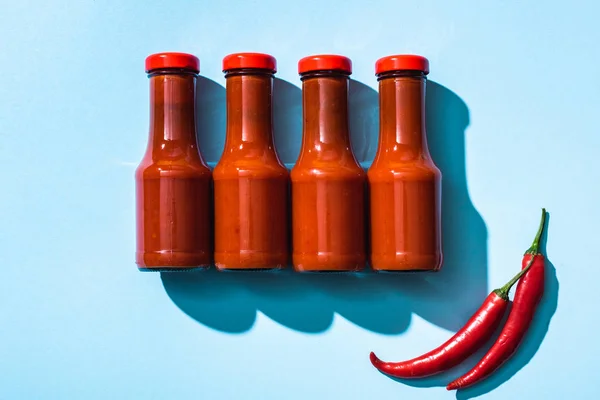 Top view of chill peppers and tomato sauce in bottles on blue background — Stock Photo