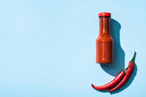 Top view of chili sauce and raw chili peppers on blue background — Stock Photo