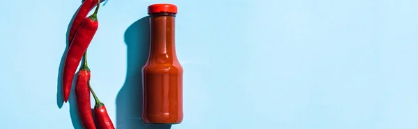 Top view of tasty chili sauce with chili peppers on blue background, panoramic shot — Stock Photo