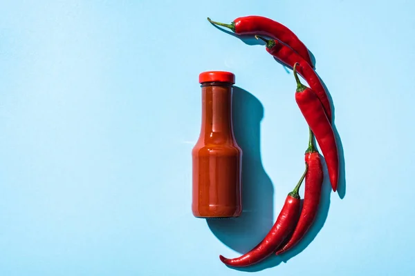 Vista dall'alto di peepers peperoncino biologico accanto salsa di pomodoro in bottiglia su sfondo blu — Foto stock