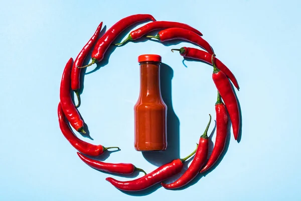Vue du dessus du cadre rond de piments autour de la bouteille avec sauce chili savoureuse sur fond bleu — Photo de stock