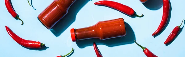 Top view of two bottle with chili sauce and ripe chili peppers on blue background, panoramic shot — Stock Photo