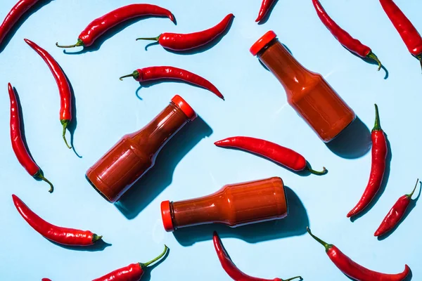 Top view of ripe chili peppers with chili sauce in bottles on blue background — Stock Photo