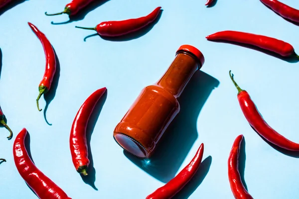 Flasche mit leckerer Chilisoße und Chilischoten auf blauem Hintergrund — Stockfoto