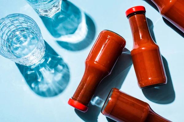 Vista superior de dos vasos de agua con salsa de tomate en botellas sobre fondo azul - foto de stock