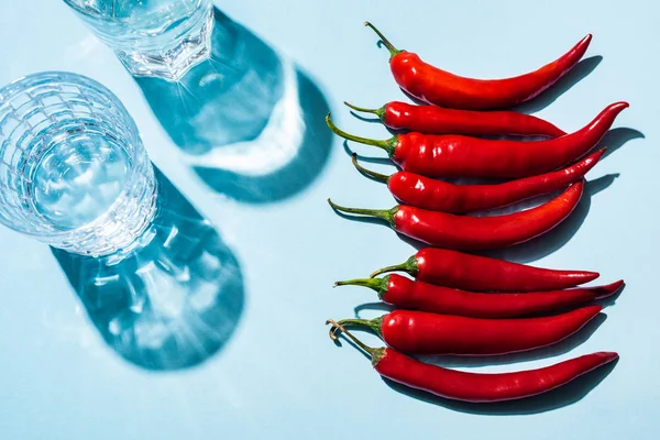 Draufsicht auf frische Chilischoten neben Wassergläsern auf blauem Hintergrund — Stockfoto