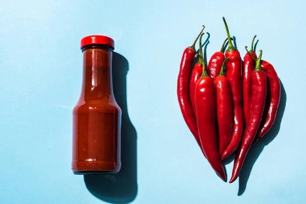 Top view of organic chili peppers and tasty chili sauce on blue surface — Stock Photo