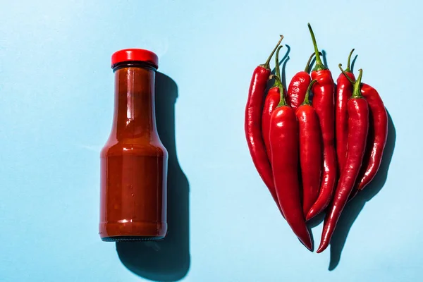 Blick von oben auf Bio-Chilischoten und leckere Chilisoße auf blauer Oberfläche — Stockfoto