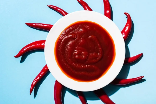 Vista dall'alto del piatto con gustosa salsa di peperoncino e peperoncini su sfondo blu — Foto stock