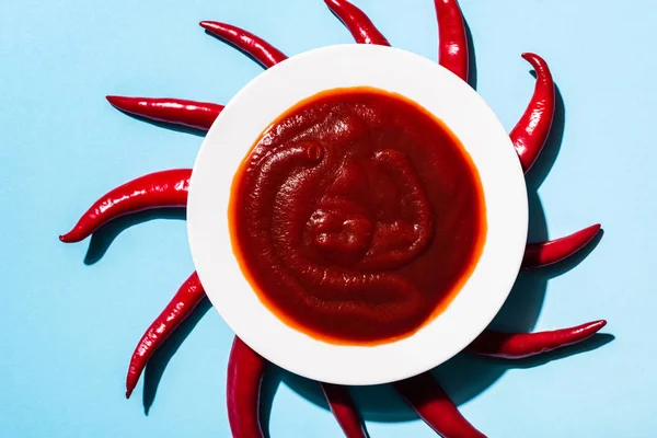 Vista superior del plato con sabrosa salsa de chile y chiles sobre fondo azul — Stock Photo