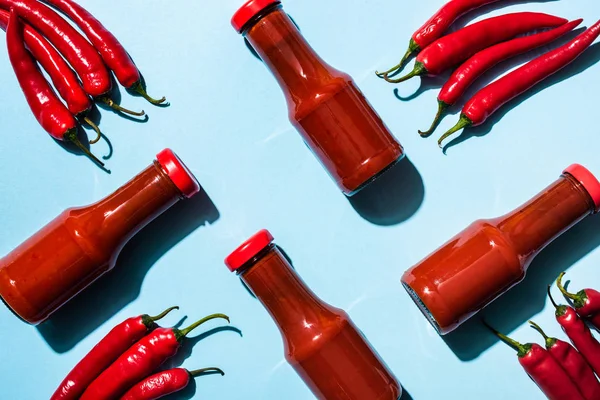 Vista superior de garrafas com molho de pimenta ao lado de pimentas na superfície azul — Fotografia de Stock