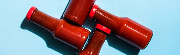 Vista superior de garrafas com molho de tomate saboroso na superfície azul, tiro panorâmico — Fotografia de Stock