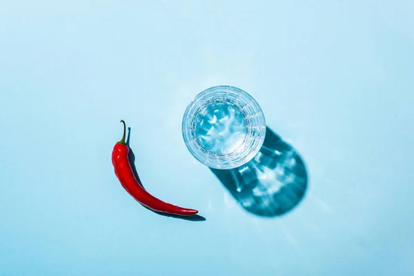 Glas mit Wasser und reifer Chilischote auf blauem Hintergrund — Stockfoto