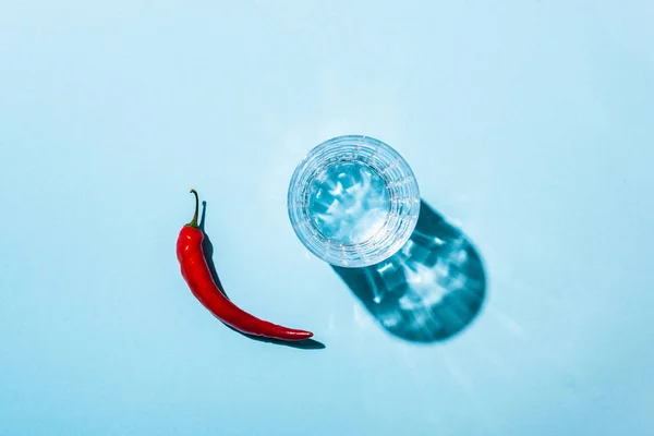 Vue du dessus du verre avec de l'eau et du piment mûr sur fond bleu — Photo de stock